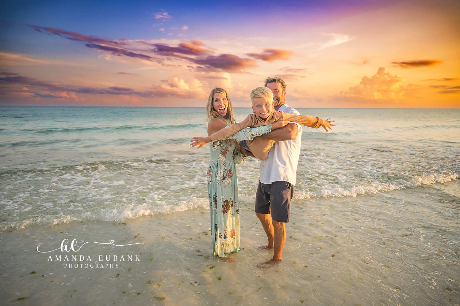 Parents Swinging Their Son | Family Photographer in Tampa, Florida Family beach portraits in Tampa, FL showing parents swinging their son between them in the shallows at golden hour.