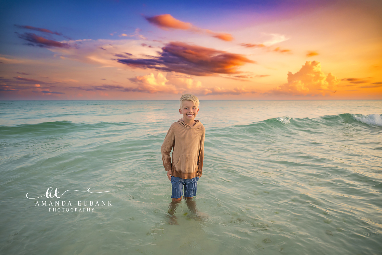 Boy at the Water’s Edge — Tampa Bay Children’s Photography A young boy standing at the water's edge under a wide gold and purple sky at a beach kids session in Tampa, FL.