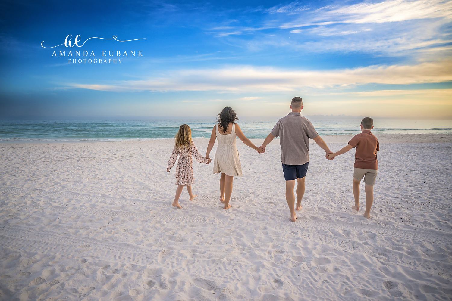 Family Walking Out to Sea | Tampa Family Photographer A family of four walking hand in hand into the shallows with their backs to the camera during a Tampa family photography session.