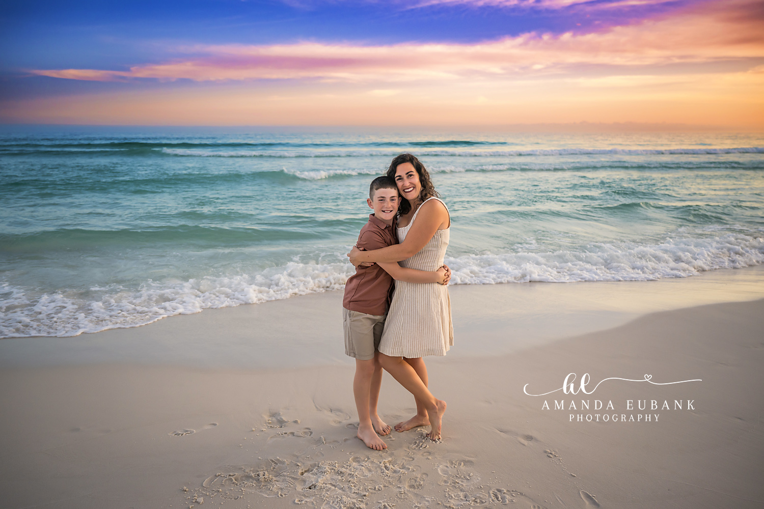 Mother and Son on the Shoreline | Family Photographer in Tampa, Florida Family beach portraits in Tampa, FL showing a mother and her son holding each other on the shoreline at pastel sunset.