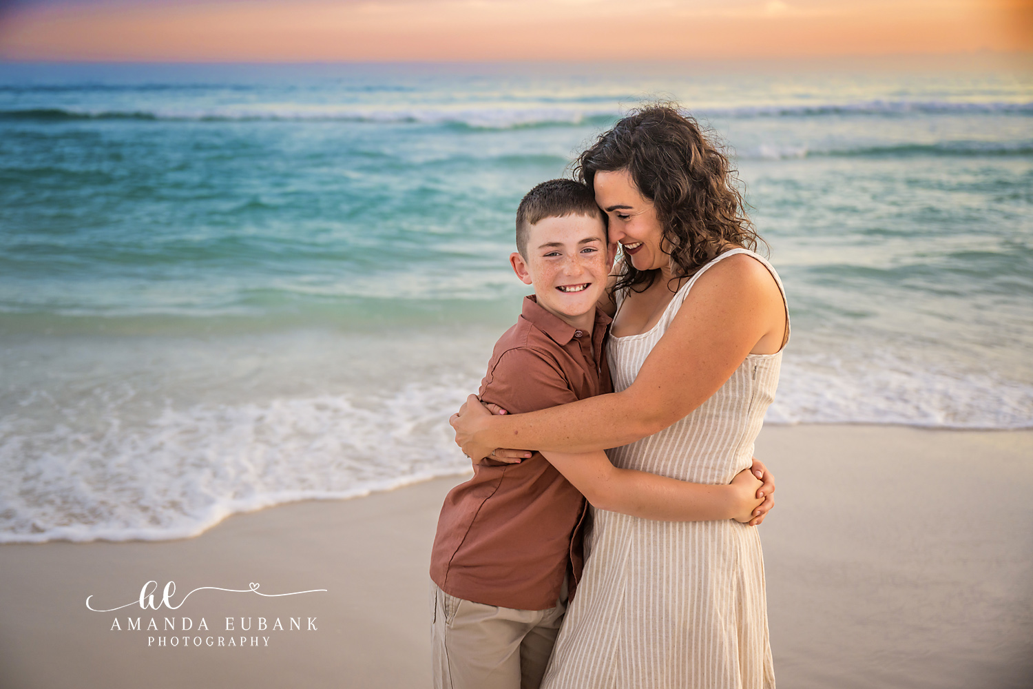 Mother and Son Hug in the Surf — Tampa Bay Family Portraits A boy hugging his mother at the water's edge as the sky turns coral — beach family photography in Tampa Bay.