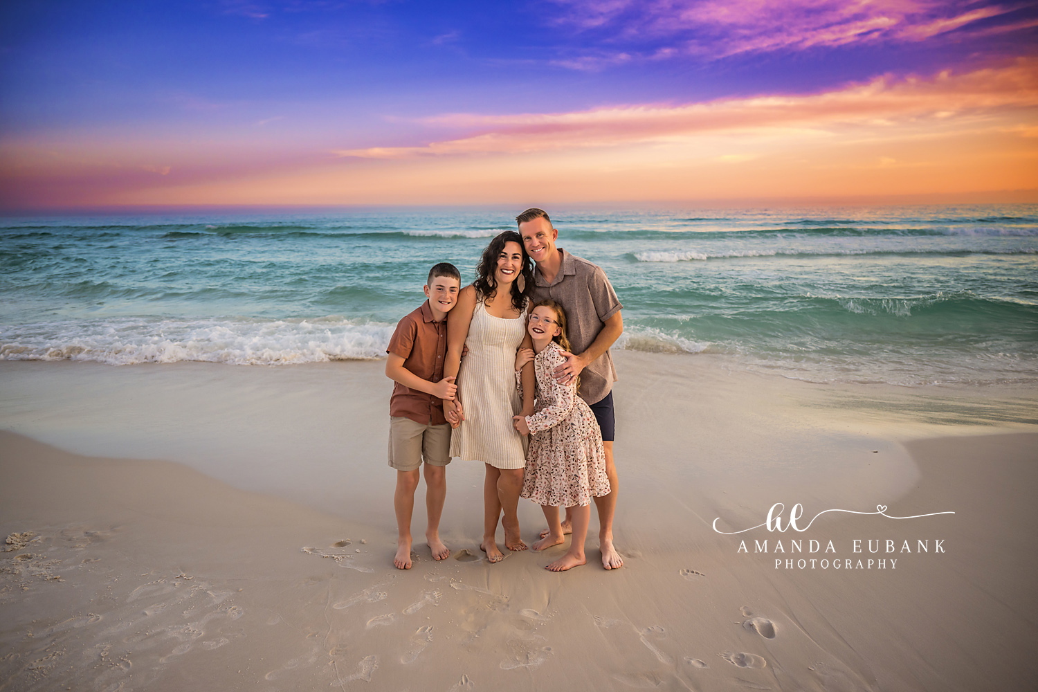 Family of Five Under a Painted Sky | Family Photographer in Tampa, Florida Family beach portraits in Tampa, FL showing a family of five standing close on the sand beneath a purple and gold sunset.