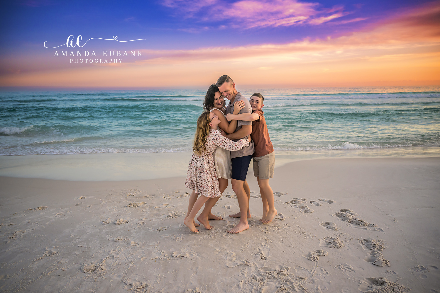Family of Five Holding Close | Tampa Beach Family Photography Tampa family photographer captures a family of five holding each other on the sand beneath purple and gold clouds.