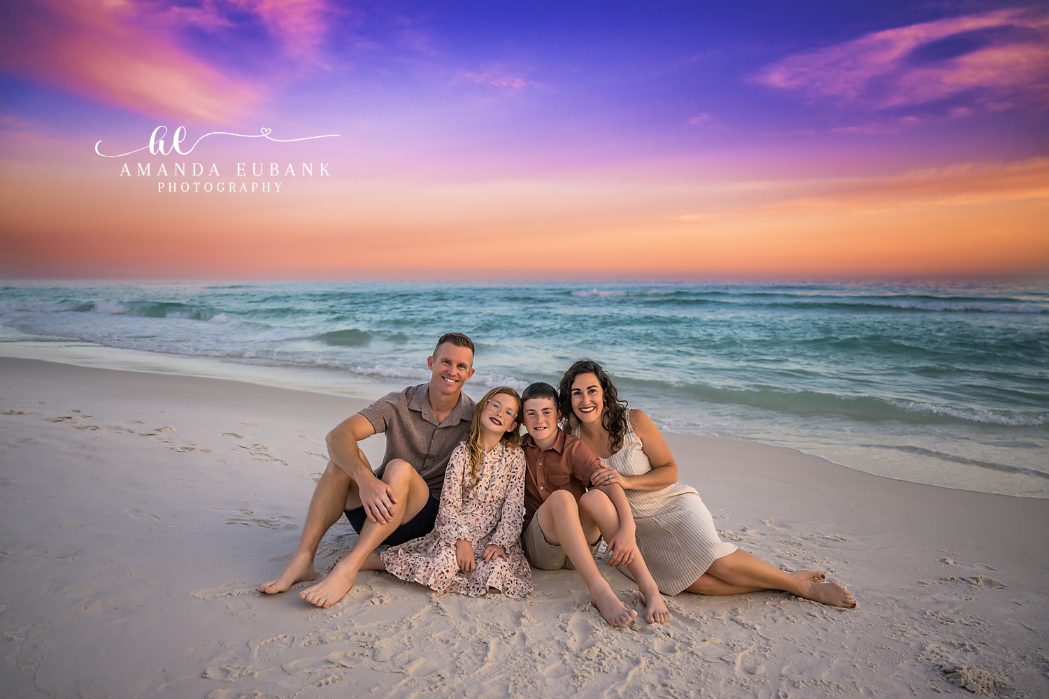 Family Seated at the Shoreline | Tampa Family Photographer A family of five seated on the sand near the shoreline beneath a purple sky during a Tampa family photography session.