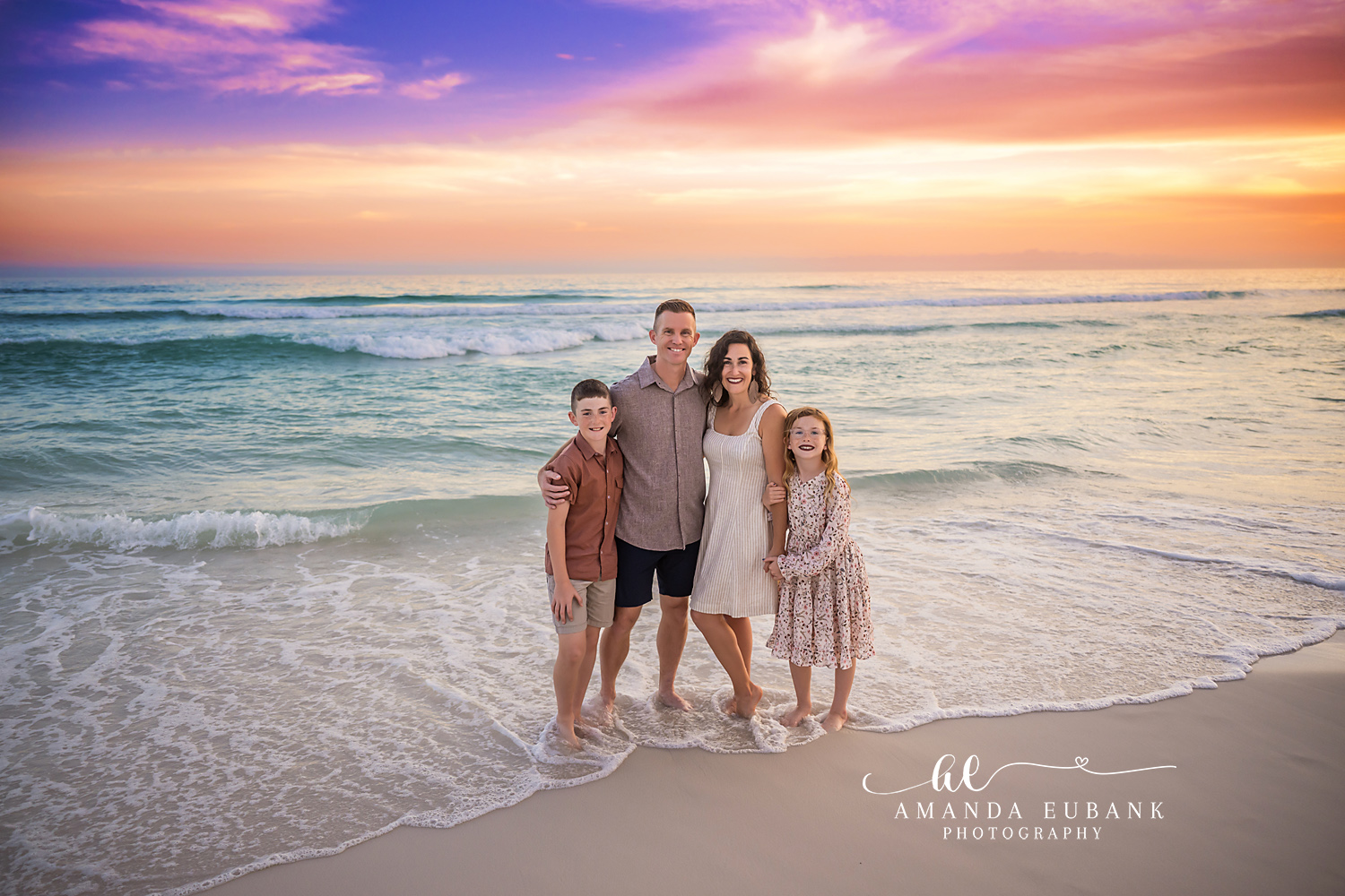 Family of Four in Warm Tones — Tampa, FL Family Session A family of four standing at the water's edge in rust and cream at sunset at a beach family session near Tampa, Florida.