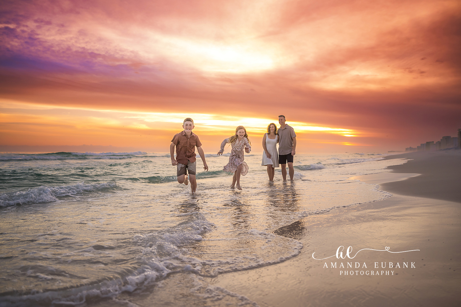 Family Wading Into the Gulf — Tampa Bay Family Portraits A family of four wading hand in hand into the Gulf beneath a fiery sunset — beach family photography in Tampa Bay.