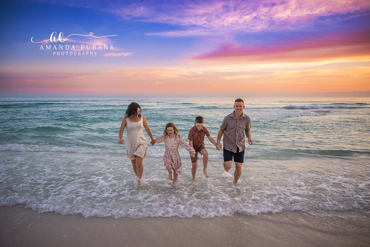 Family Walking Into the Waves | Family Photographer in Tampa, Florida Family beach portraits in Tampa, FL showing a family of four walking hand in hand into the waves with their backs to the camera.