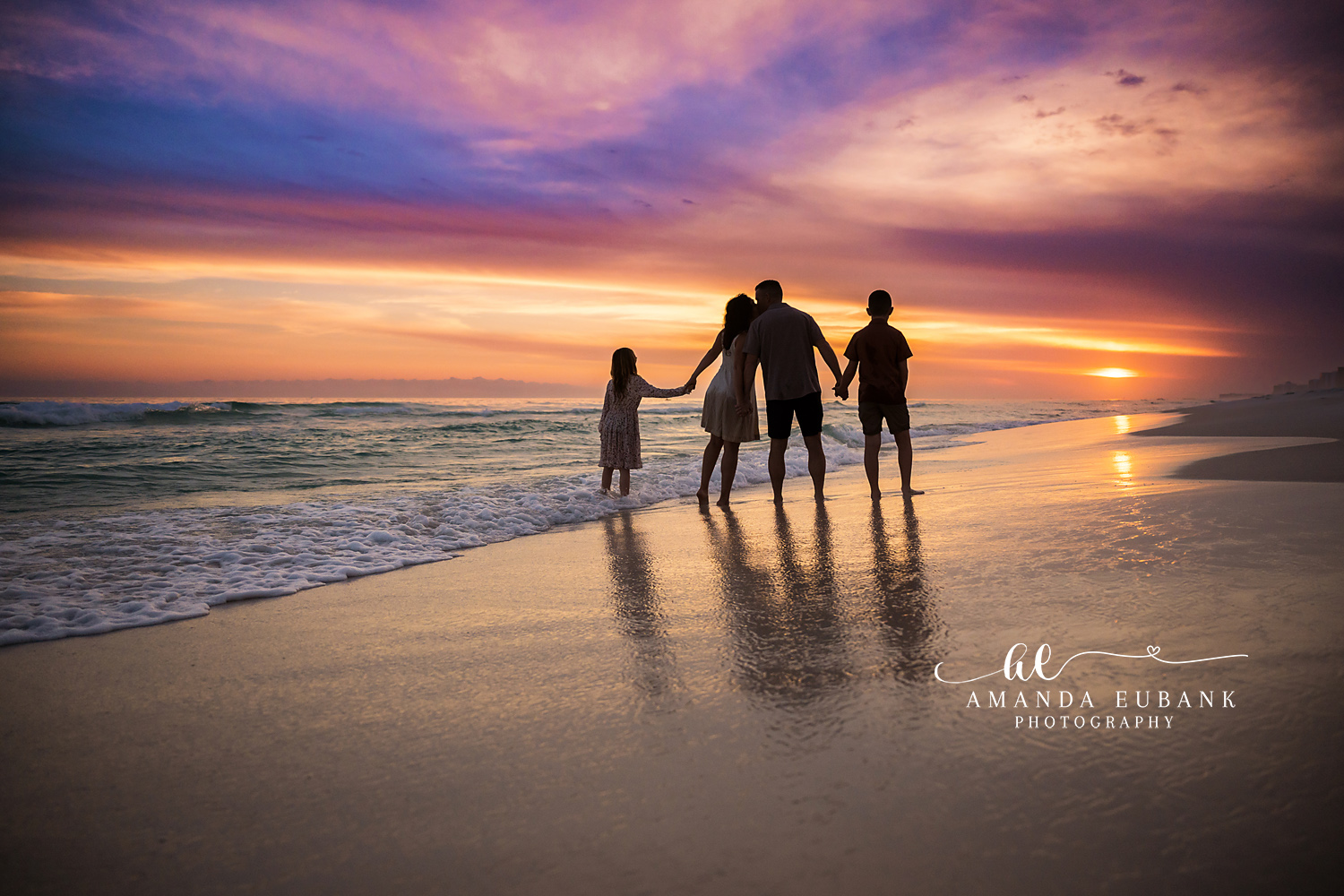 Silhouetted Family Walk | Tampa Family Photographer A family of four silhouetted on mirror-wet sand beneath a burning sunset during a Tampa family photography session.