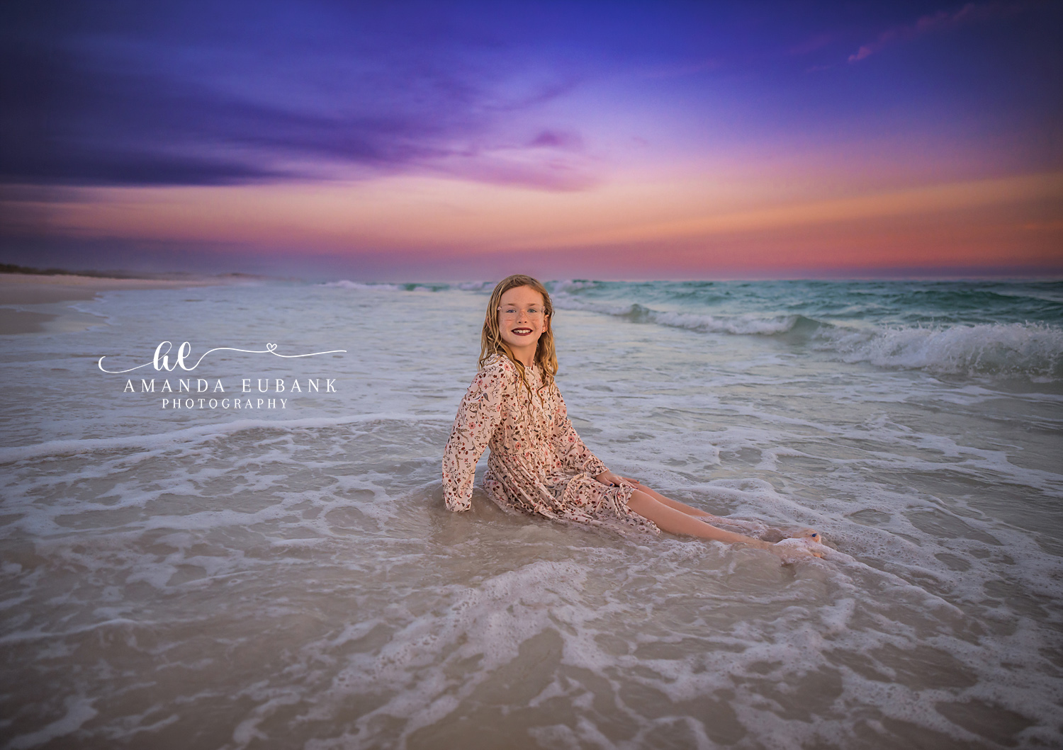 Girl Sitting in the Surf — Tampa Bay Children’s Photography A girl in a floral dress sitting in the shallow surf under a purple sky at a beach kids session in Tampa, FL.