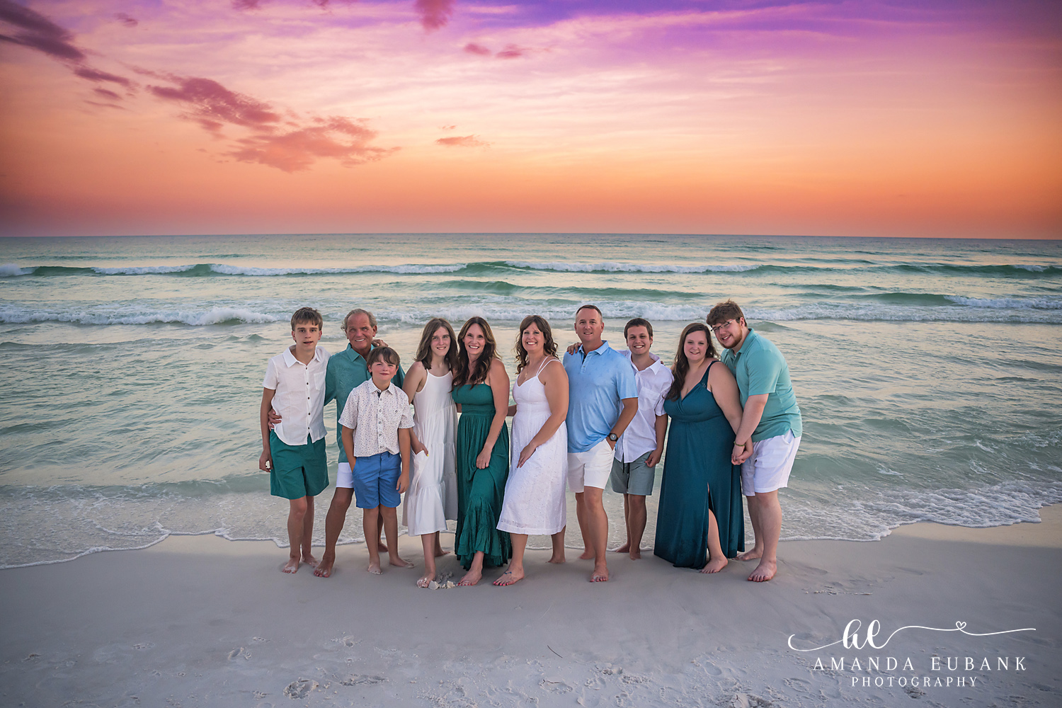 Large Family Group at Sunset | Tampa Extended Family Photographer An extended family of twelve gathered on the sand in teal beneath a coral sky during an extended family photography session in Tampa, Florida.