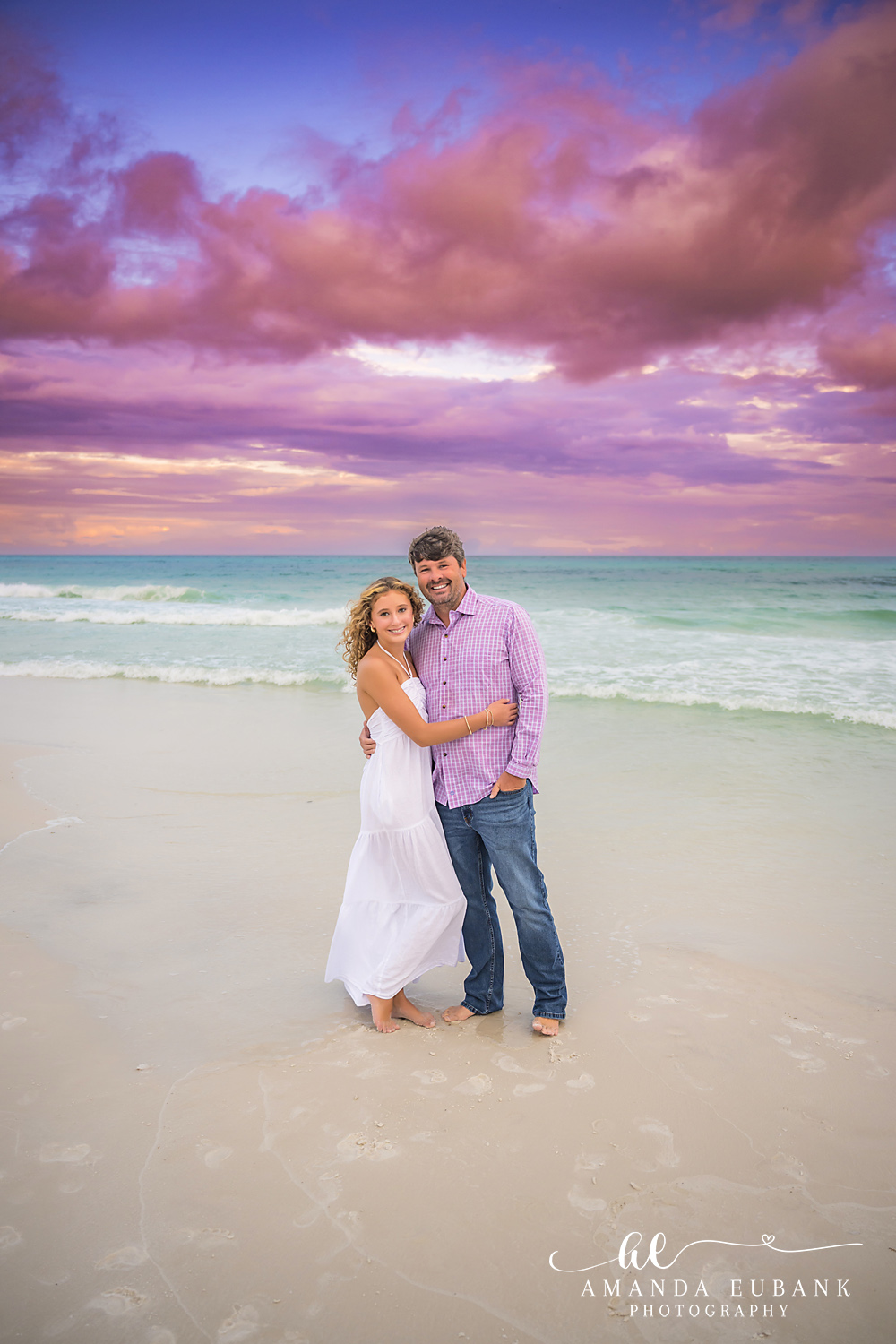 Parents Embracing on the Sand — Tampa, FL Couples Session A couple holding each other on the sand in pink and white under purple clouds at a beach couples session near Tampa, Florida.