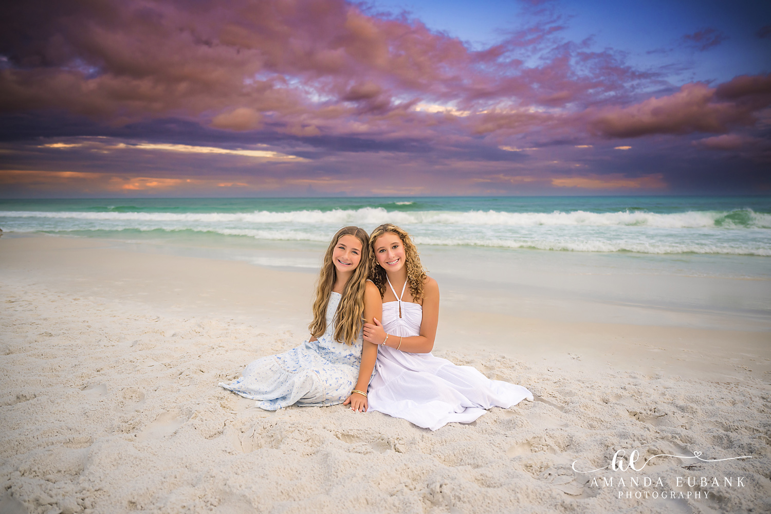 Sisters Sitting on the Beach | Tampa Family Photographer Two sisters sitting together on the sand in white and blue at dusk during a Tampa family photography session.
