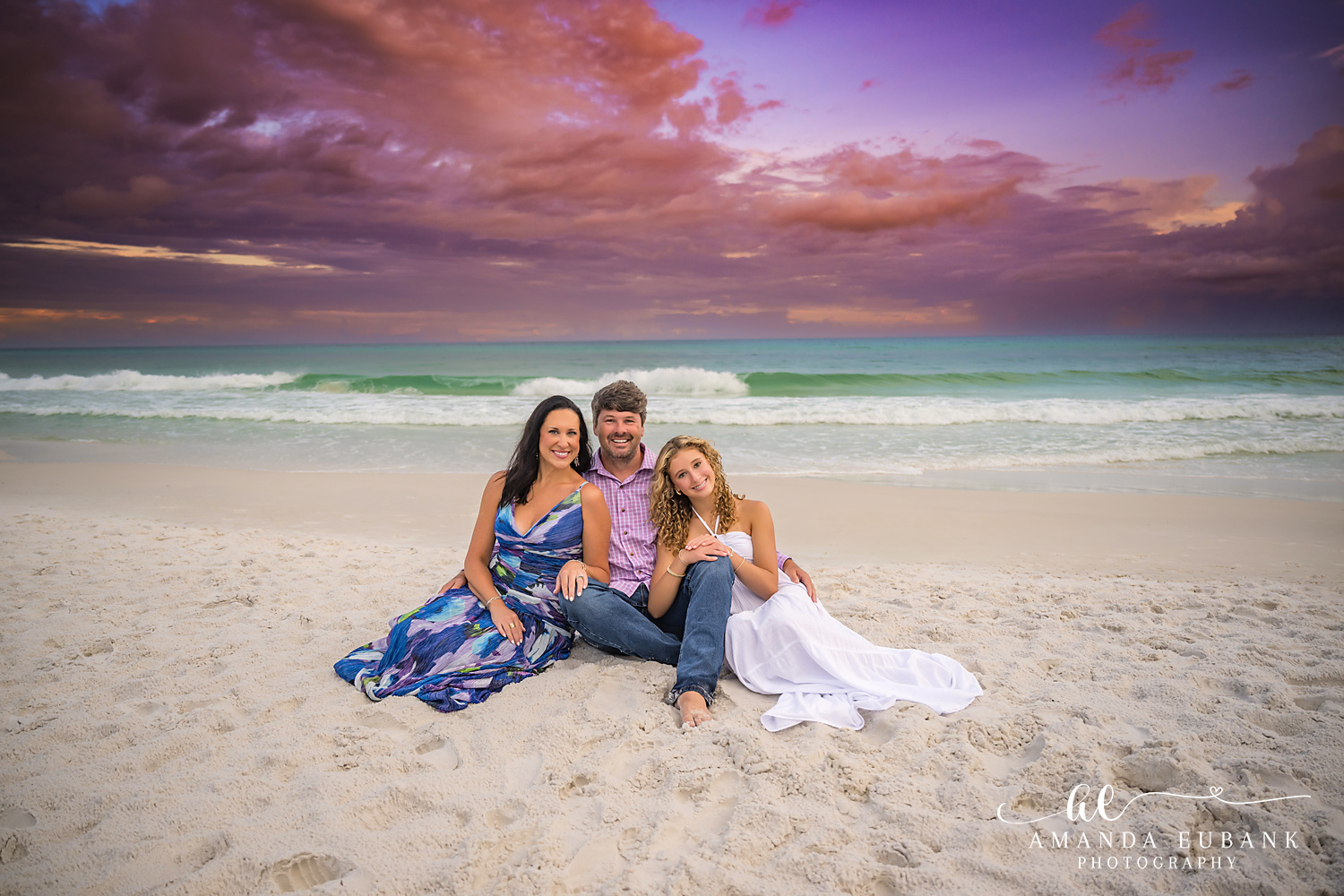 Family Portrait on the Sand | Family Photographer in Tampa, Florida Family beach portraits in Tampa, FL showing a family of four seated on the beach in blue and white beneath purple clouds.