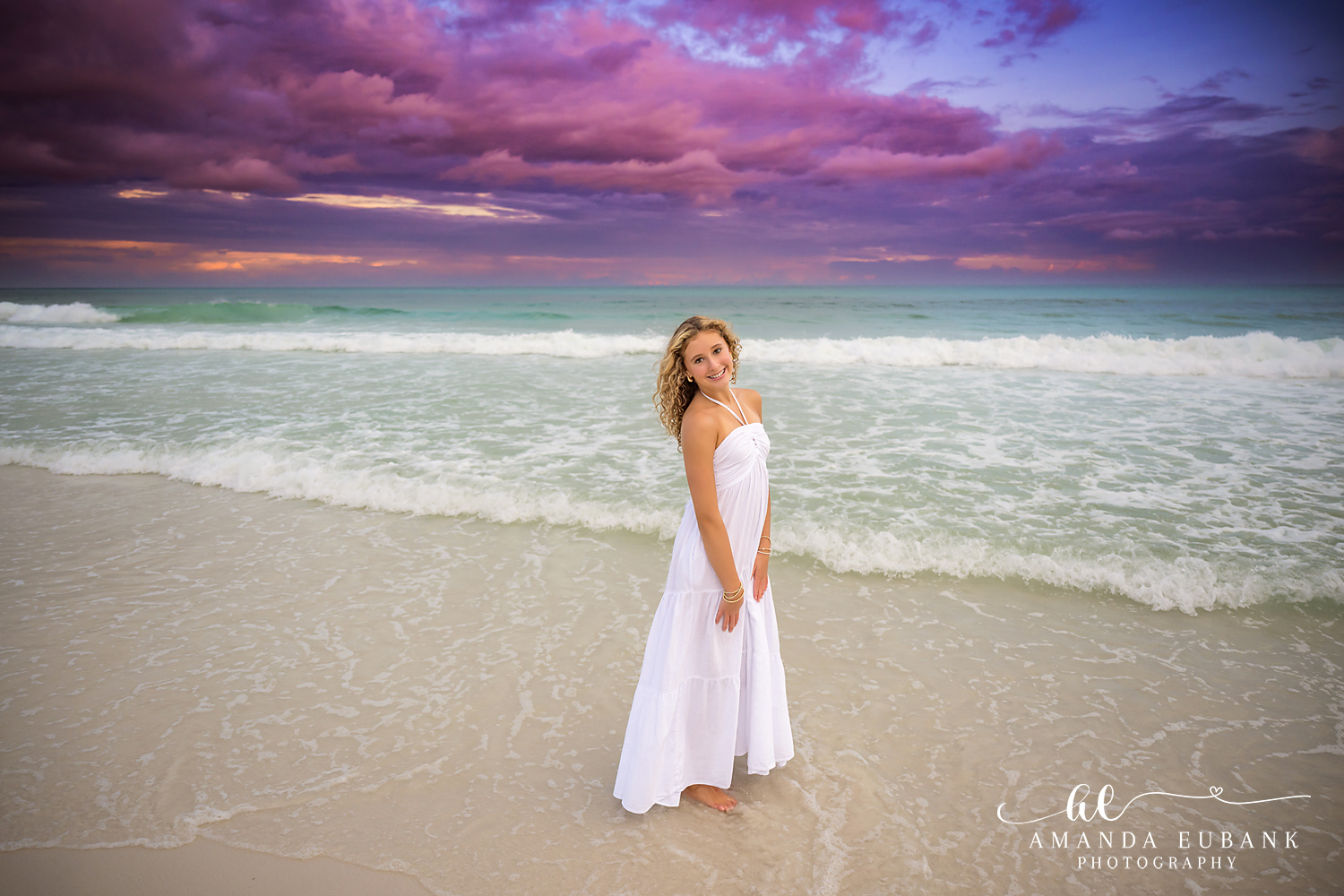 White Gown at the Water’s Edge — Tampa Bay Family Portraits A young woman in a flowing white gown standing at the water's edge at dusk — beach family photography in Tampa Bay.
