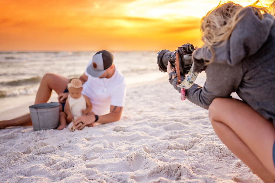 Behind the scenes of a photographer lying on the sand to photograph a family with a baby at sunset in Tampa, FL.