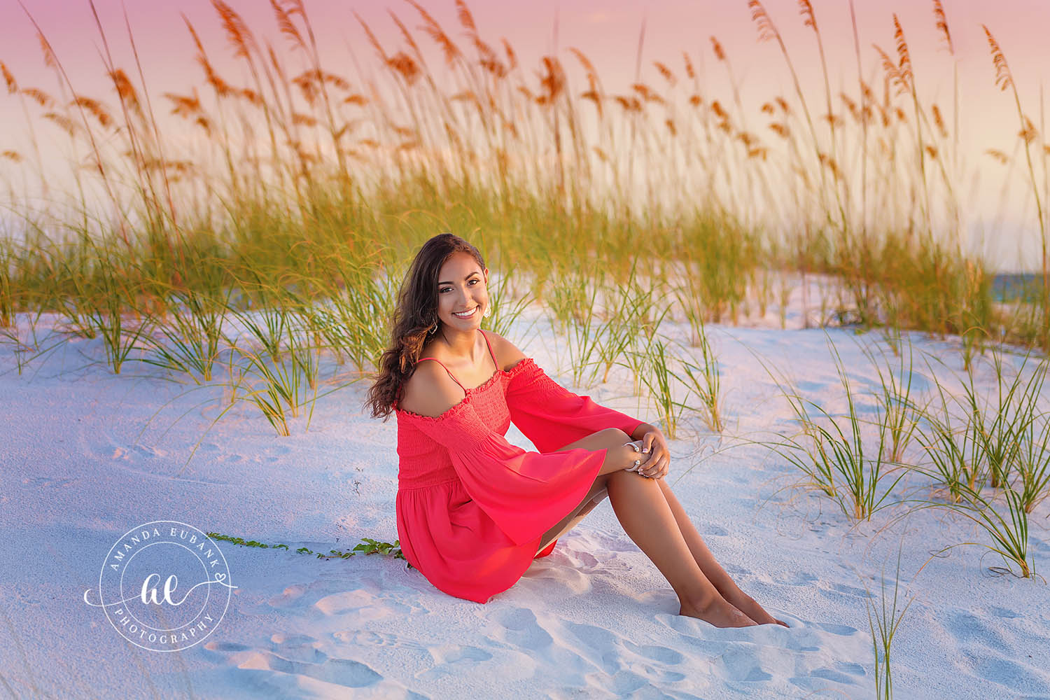 Red Dress in the Sea Oats | Beach Senior Session in Tampa, Florida Senior pictures in Tampa Bay showing a senior in a red dress seated in the dunes surrounded by golden sea oats.