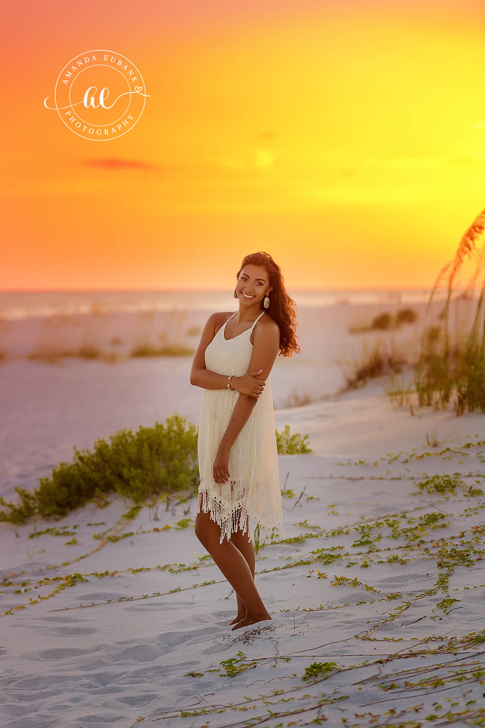 Senior in the Dunes at Golden Hour | Tampa Senior Photographer A senior in a white dress walking through the dunes as the sky blazes gold during a senior portrait session in Tampa, Florida.