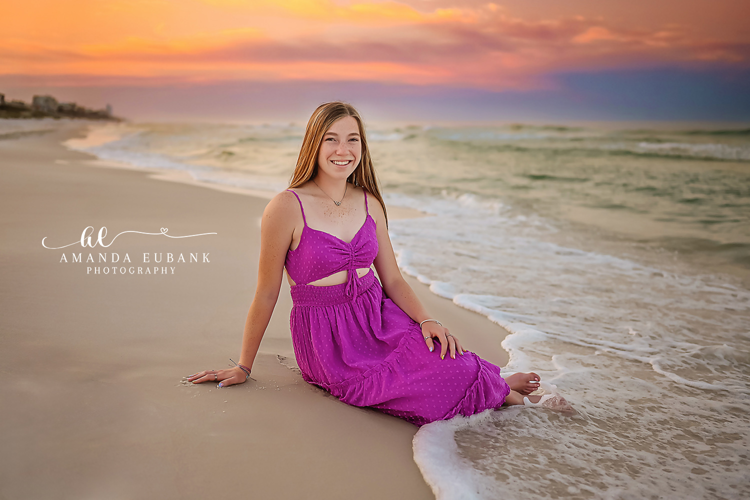 Magenta Dress on the Beach | Tampa Senior Photographer A senior in a magenta dress seated on the sand as waves wash in behind her during a senior portrait session in Tampa, Florida.