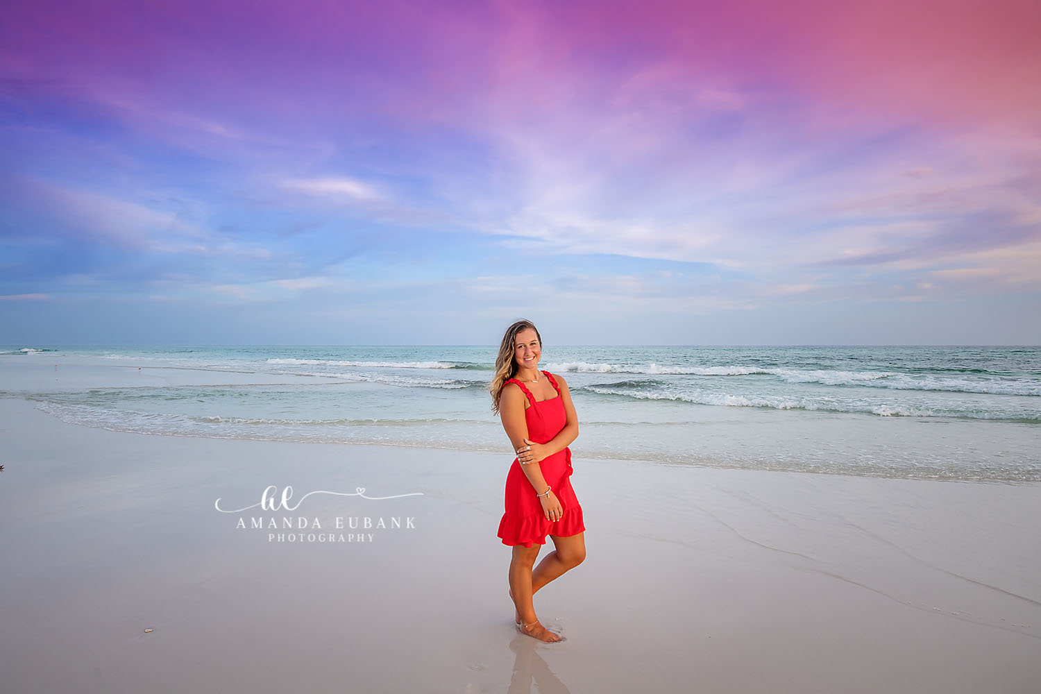 Red Dress on the Shoreline — Tampa Bay Senior Photography A senior in a red dress standing in the shallow surf under a wide blue sky at a beach senior session in Tampa, FL.