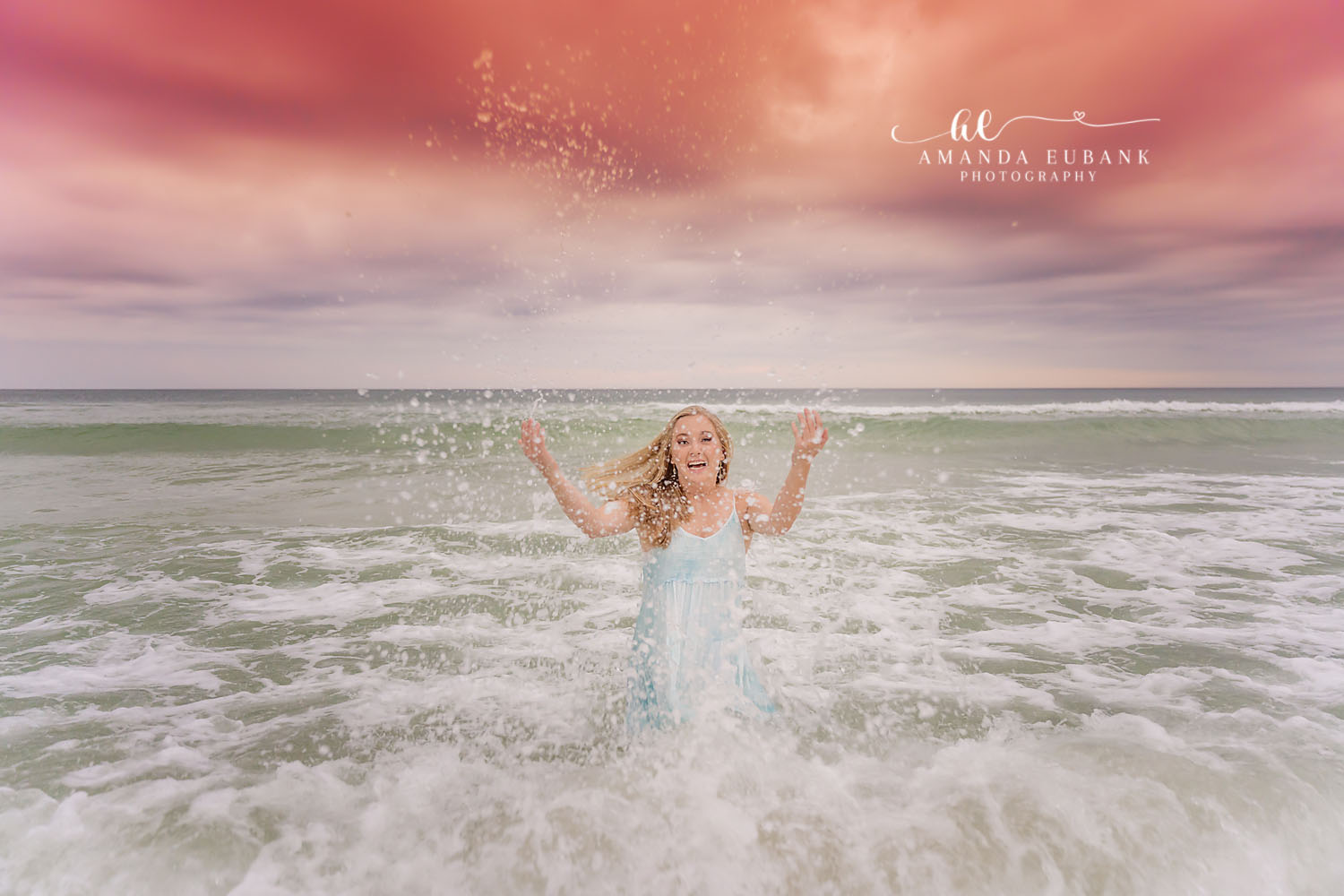Splashing in the Waves | Tampa Senior Photographer A senior in a blue dress splashing in the breaking waves with arms raised during a senior portrait session in Tampa, Florida.