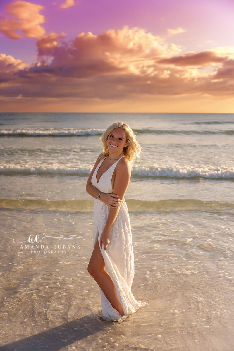 White Dress in the Shallows | Senior Portraits in Tampa, FL Tampa senior photographer captures a senior in a long white dress standing in the shallow surf at pastel dusk.