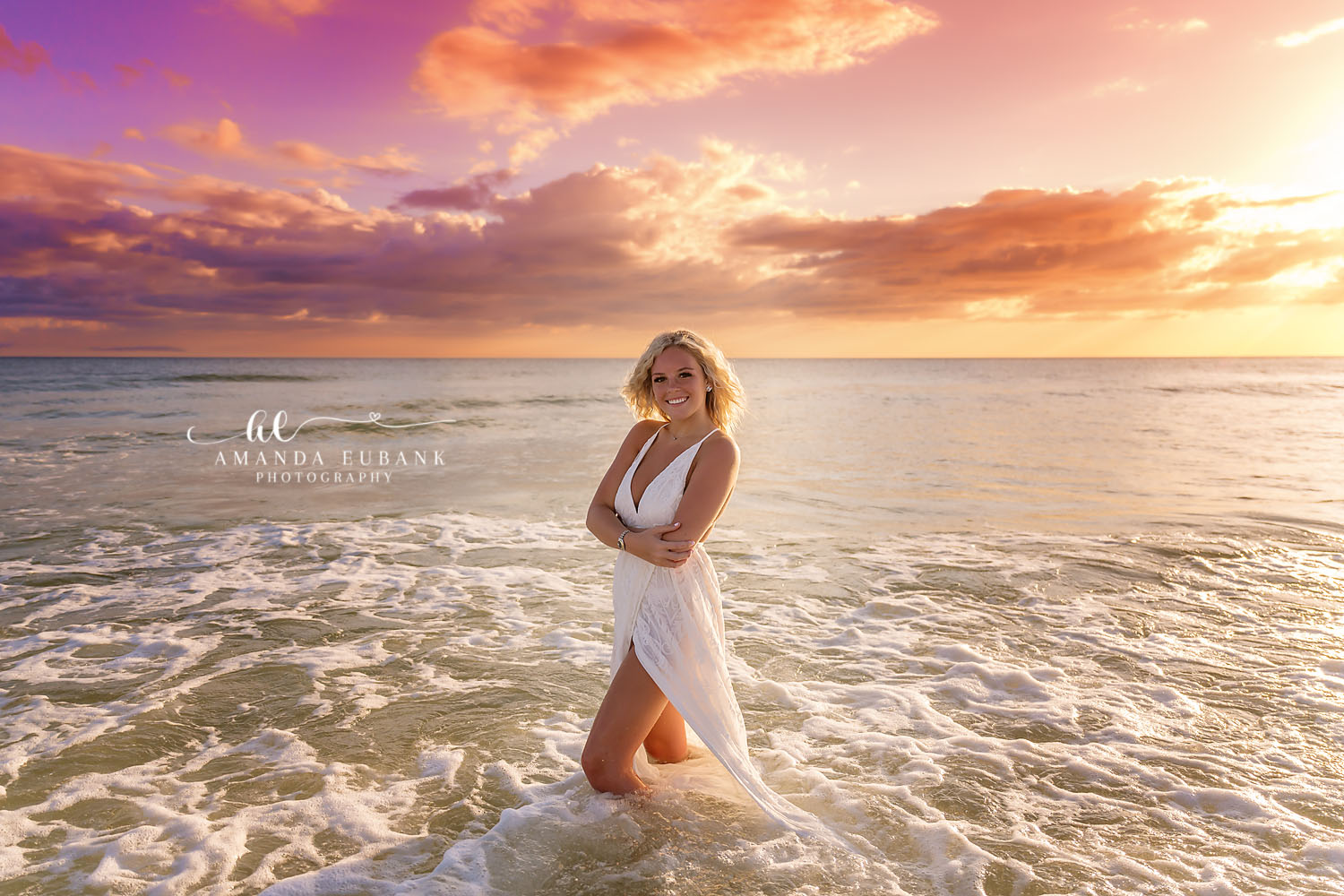 Golden Hour Senior Session | Beach Senior Session in Tampa, Florida Senior pictures in Tampa Bay showing a senior in a white dress in the surf as the sky glows gold and violet.