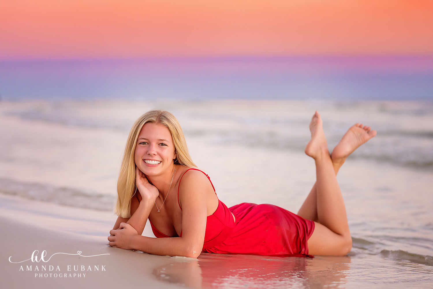 Lying on the Wet Sand | Beach Senior Session in Tampa, Florida Senior pictures in Tampa Bay showing a senior in a red dress lying on the wet sand beneath a soft pastel sky.