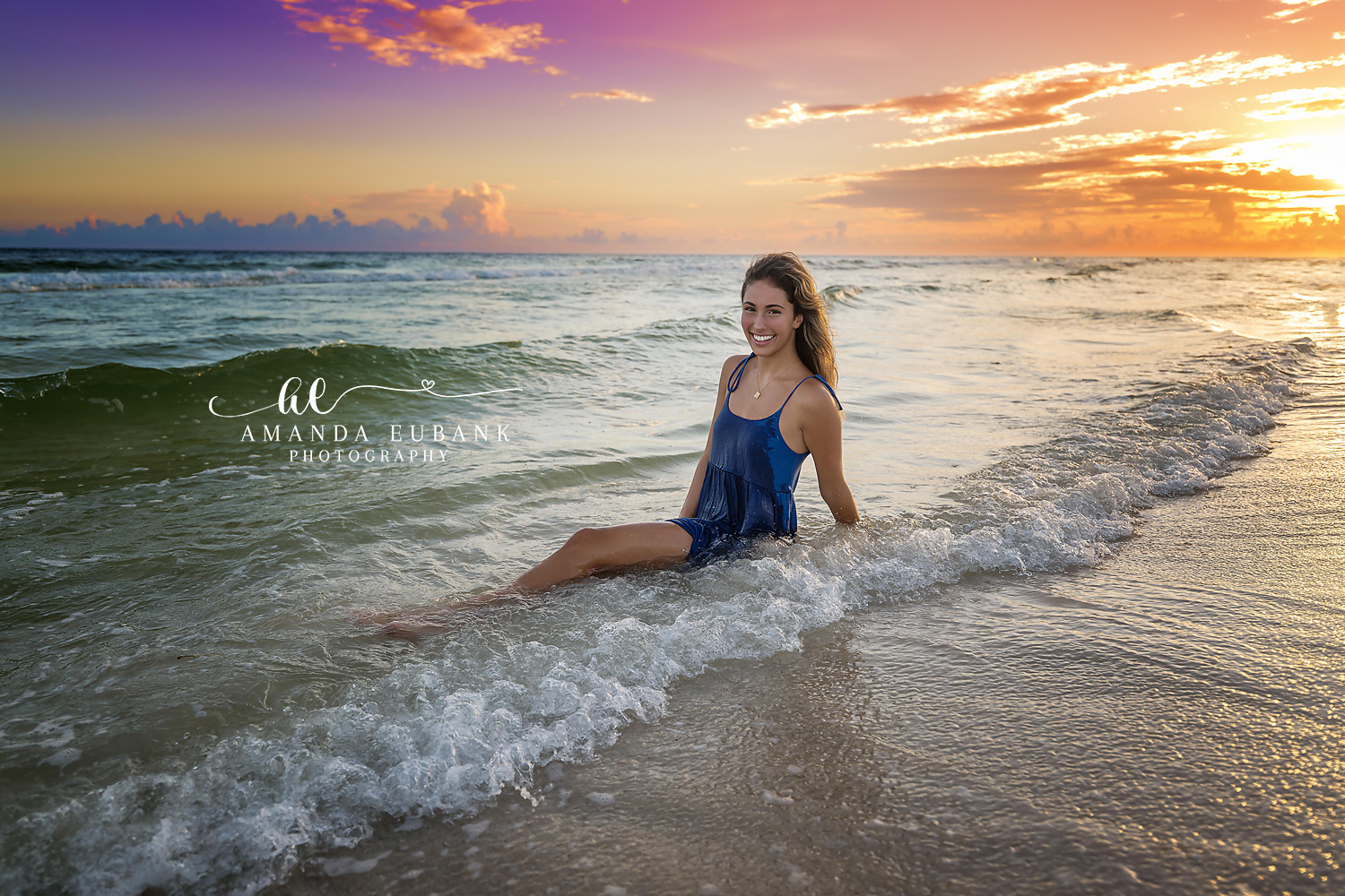 Navy Dress in the Waves | Senior Portraits in Tampa, FL Tampa senior photographer captures a senior in a navy dress seated in the surf beneath a blue and gold sky.