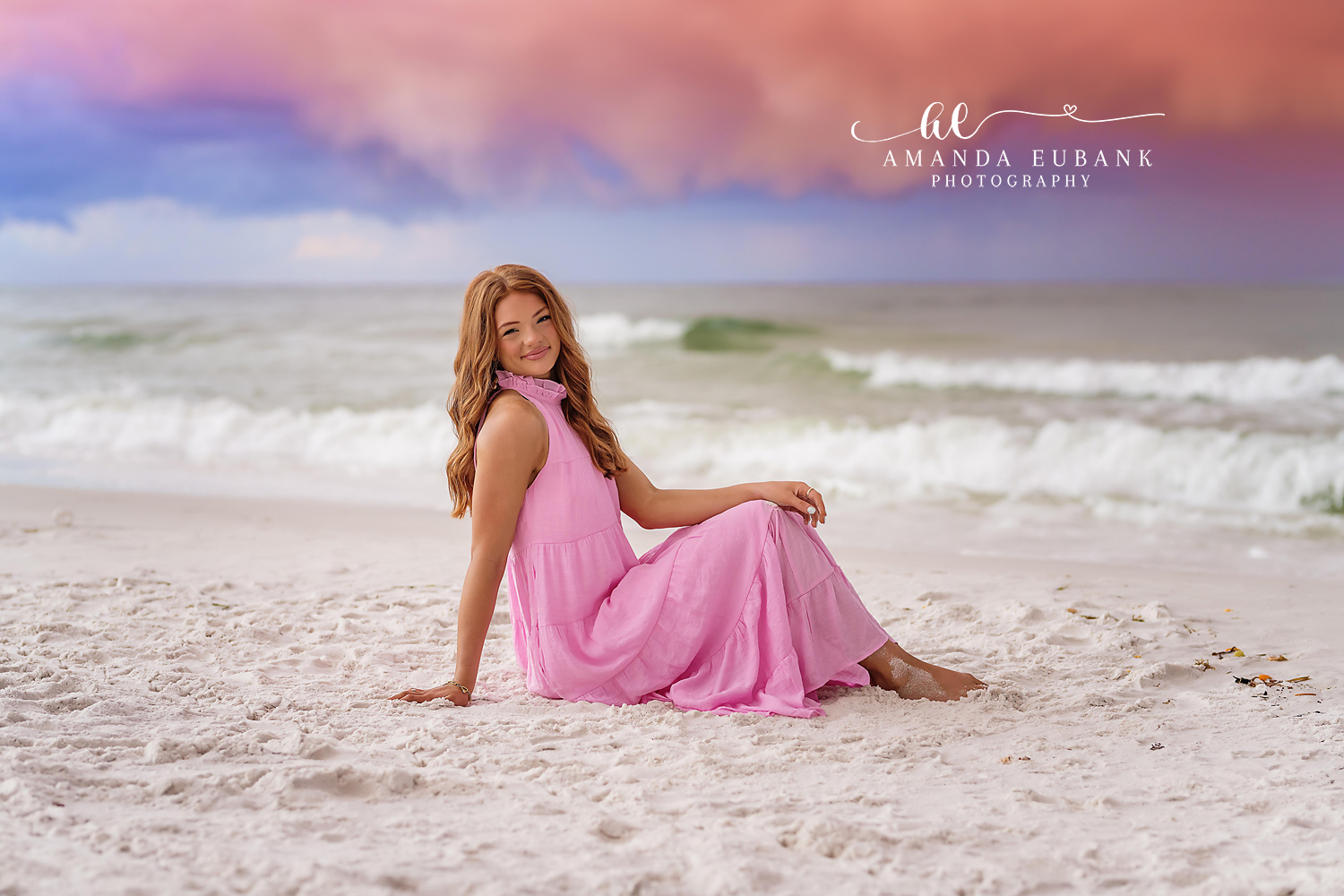 Pink Gown on the Sand | Beach Senior Session in Tampa, Florida Senior pictures in Tampa Bay showing a senior in a pink gown seated on the white sand beneath soft pastel clouds.