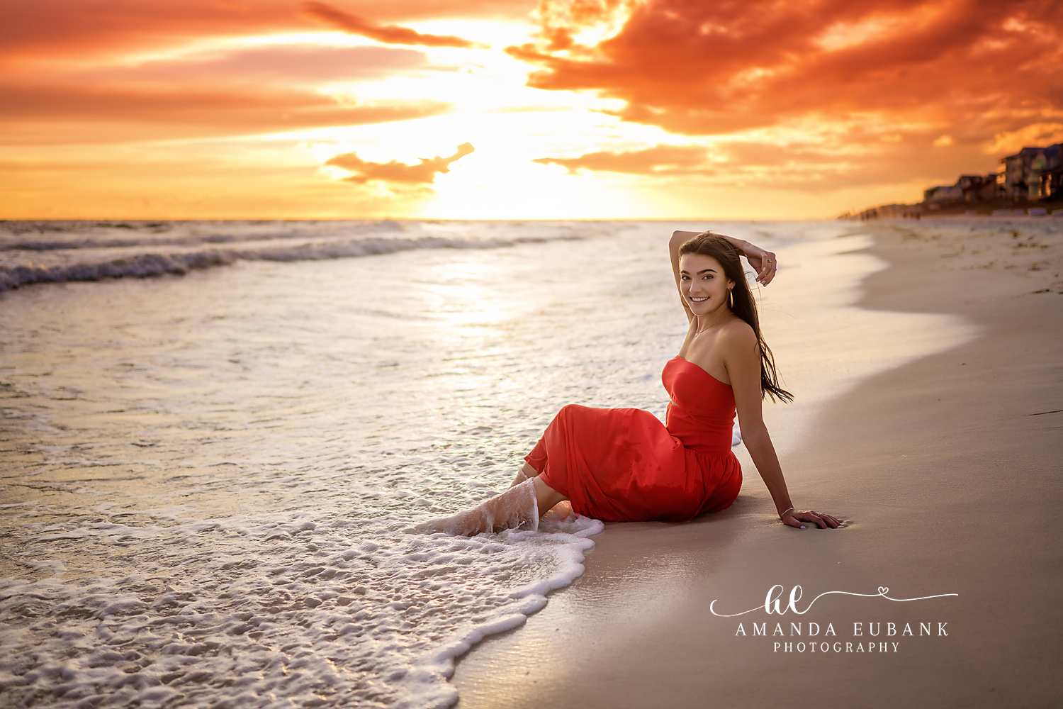 Red Gown at the Sun’s Edge | Senior Portraits in Tampa, FL Tampa senior photographer captures a senior in a red gown seated on the shoreline as the sun blazes over the water.
