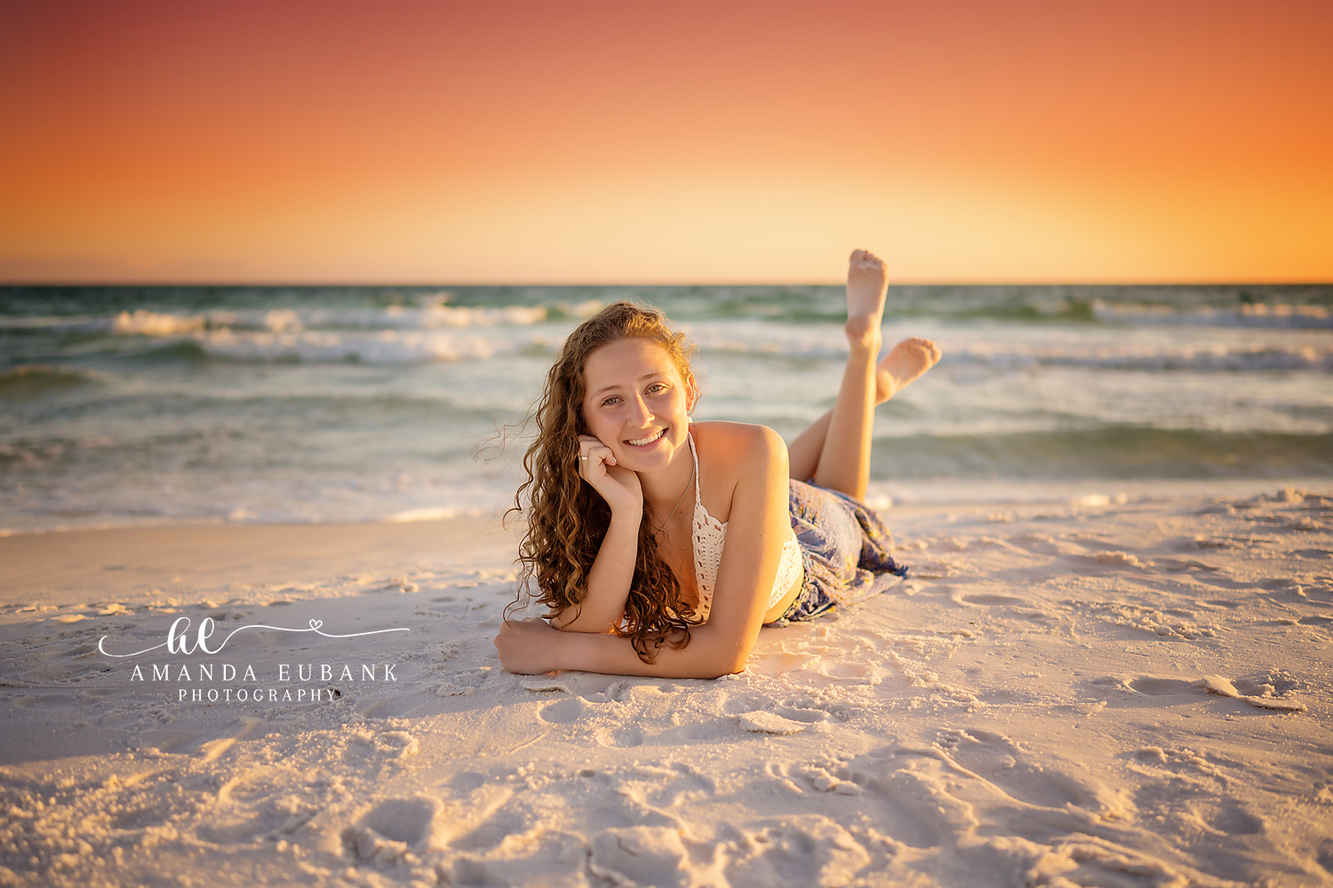Reclining at Sunset | Tampa Senior Photographer A senior in white lying on the sand as the sky glows orange over the Gulf during a senior portrait session in Tampa, Florida.
