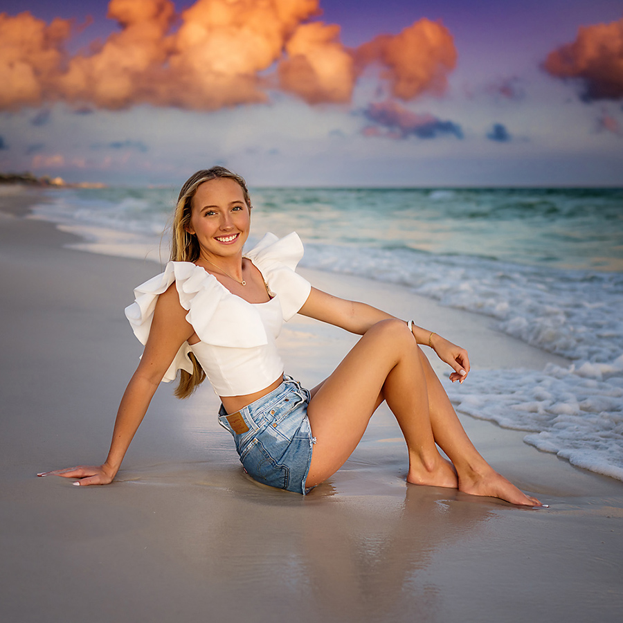 White Top and Denim Shorts | Senior Portraits in Tampa, FL Tampa senior photographer captures a senior in a ruffled white top and denim shorts seated on the wet sand.