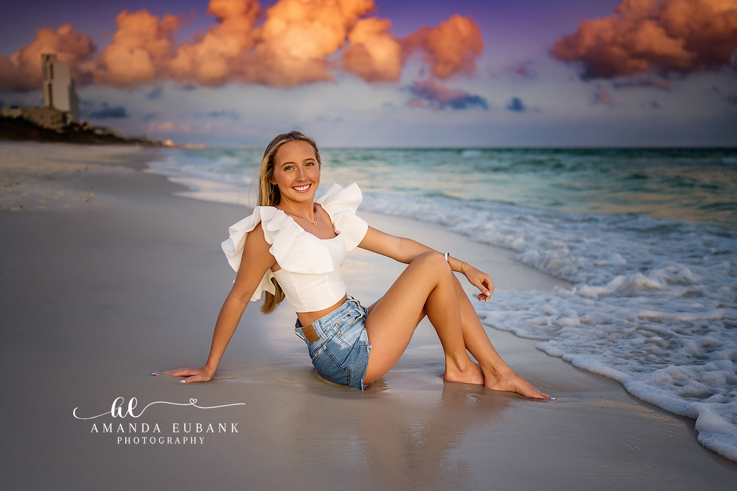 Seated Under Pink Clouds — Tampa Bay Senior Photography A senior seated on the shoreline beneath towering pink sunset clouds at a beach senior session in Tampa, FL.