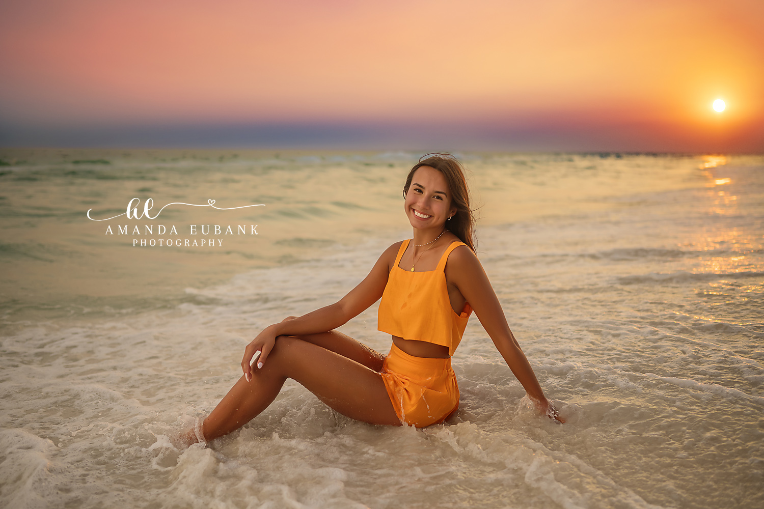 Orange Set at Sundown — Tampa Bay Senior Photography A senior in an orange two-piece seated on the wet sand as the sun meets the water at a beach senior session in Tampa, FL.