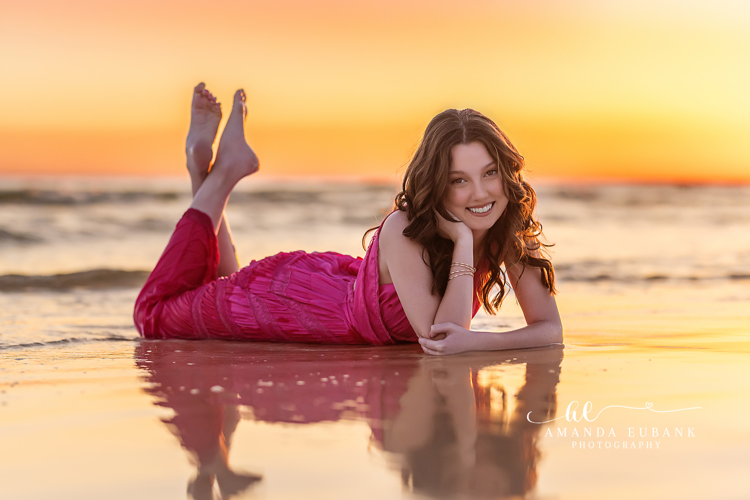 Reflections on the Shoreline | Senior Portraits in Tampa, FL Tampa senior photographer captures a senior in a pink gown lying on mirror-wet sand at golden sunset.