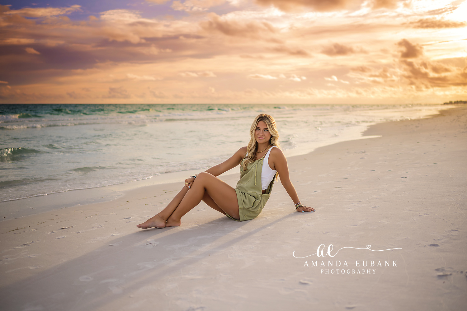 Seated on the Open Beach | Beach Senior Session in Tampa, Florida Senior pictures in Tampa Bay showing a senior in a green dress seated on the open sand beneath warm sunset clouds.