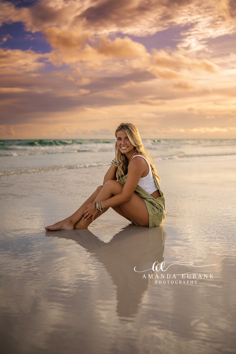 Reflected on the Wet Sand — Tampa Bay Senior Photography A senior seated on mirror-wet sand with her reflection under pastel clouds at a beach senior session in Tampa, FL.