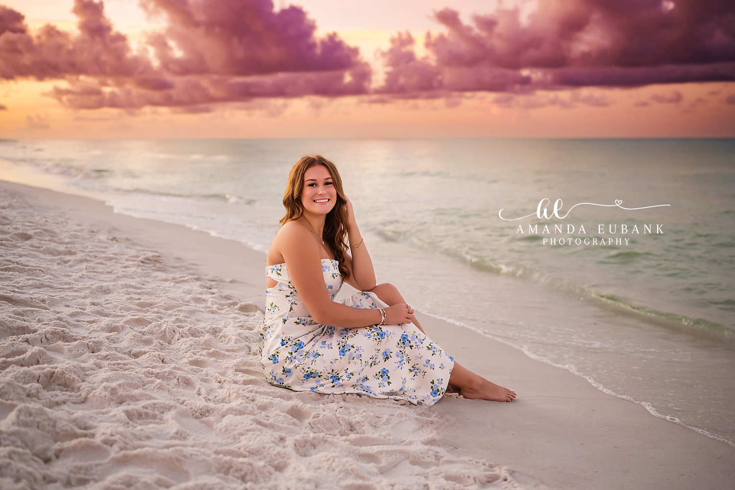 Seated Under a Pastel Sky | Beach Senior Session in Tampa, Florida Senior pictures in Tampa Bay showing a senior in a white floral dress seated on the sand beneath a pastel sky.