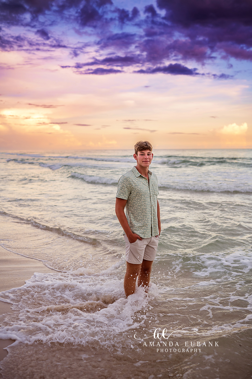Senior Guy in the Surf | Tampa Senior Photographer A senior guy standing in the shallow surf under a purple and gold sky during a senior portrait session in Tampa, Florida.