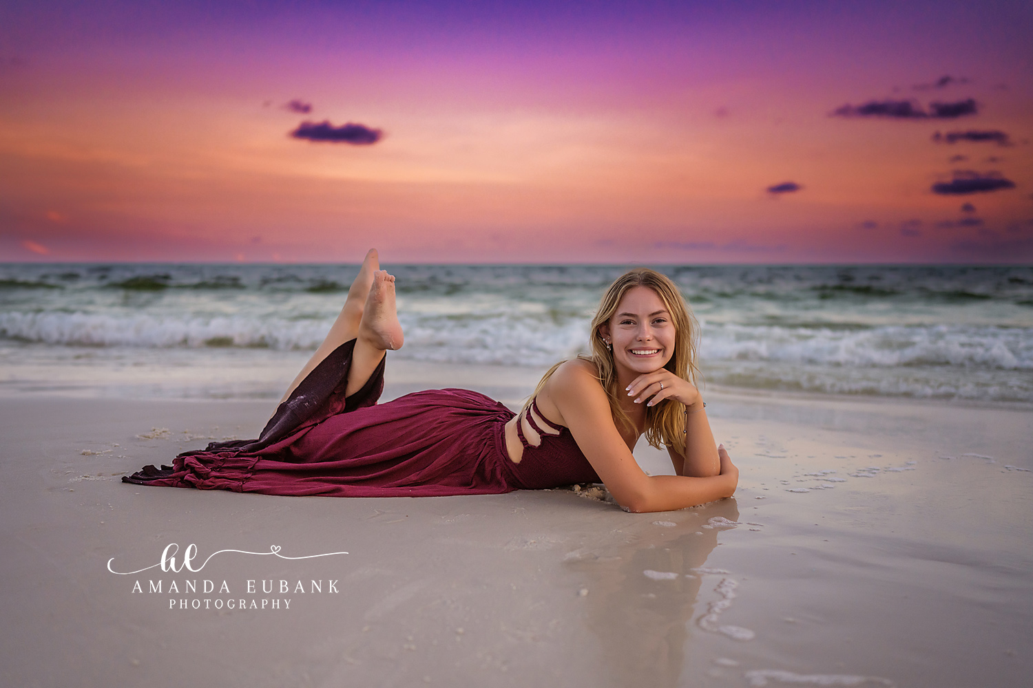 Burgundy Gown on the Wet Sand — Tampa Bay Senior Photography A senior in a burgundy gown lying on the wet sand at violet sunset at a beach senior session in Tampa, FL.