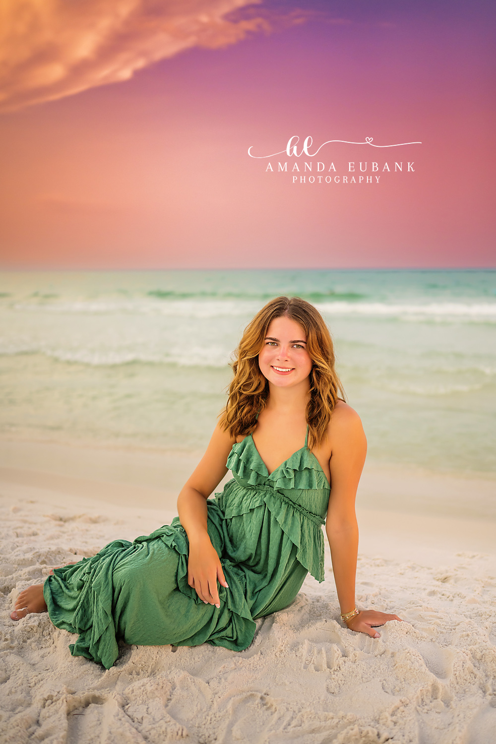 Green Gown in the Shallows | Beach Senior Session in Tampa, Florida Senior pictures in Tampa Bay showing a senior in a green gown seated in the shallow surf at pastel sunset.
