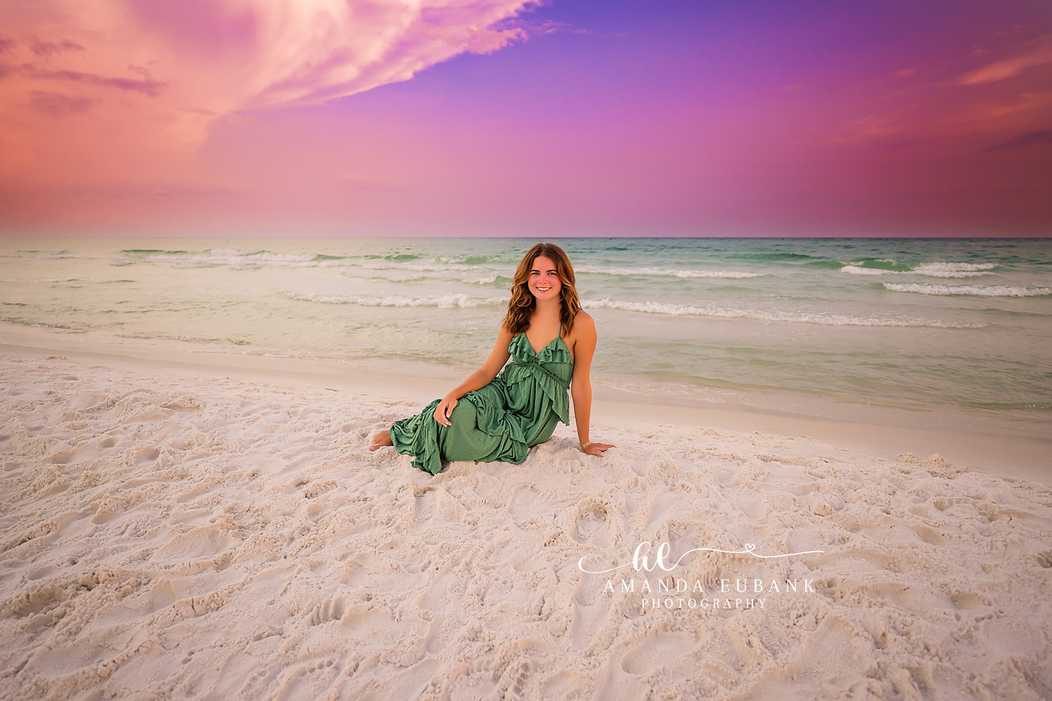 Green Gown on White Sand | Tampa Senior Photographer A senior in a green gown seated on white sand beneath a purple and pink sky during a senior portrait session in Tampa, Florida.