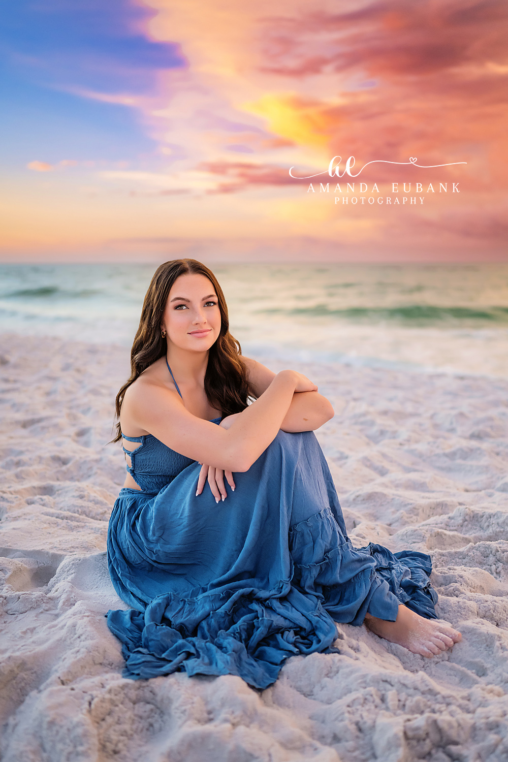 Blue Gown on the Dune | Beach Senior Session in Tampa, Florida Senior pictures in Tampa Bay showing a senior in a blue gown seated on the sand beneath a bright blue and gold sky.