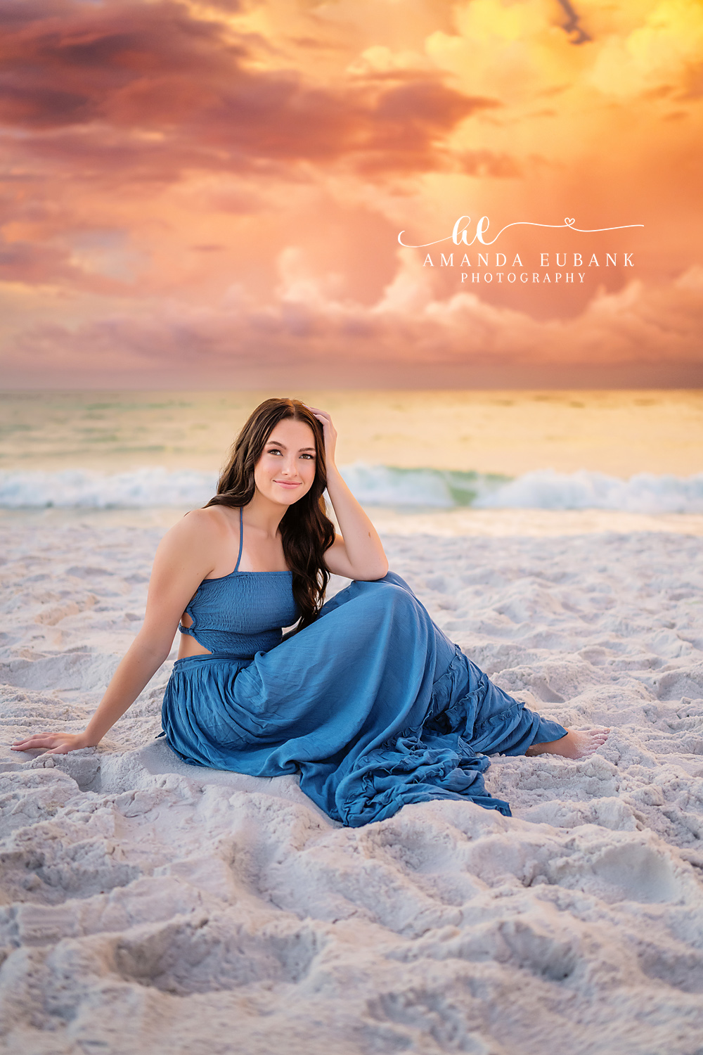 Blue Gown at Coral Sunset | Senior Portraits in Tampa, FL Tampa senior photographer captures a senior in a blue gown seated on the sand beneath coral and green sunset light.