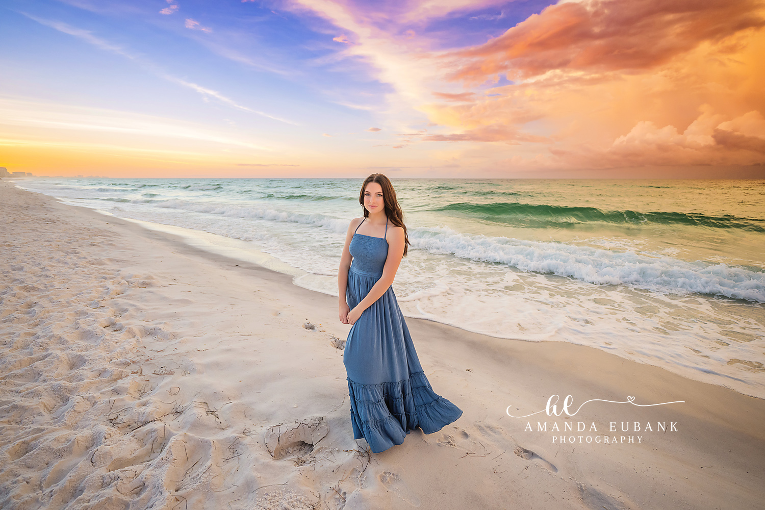 Standing in a Blue Gown | Senior Portraits in Tampa, FL Tampa senior photographer captures a senior in a blue gown standing on the sand as the sky streaks orange and blue.