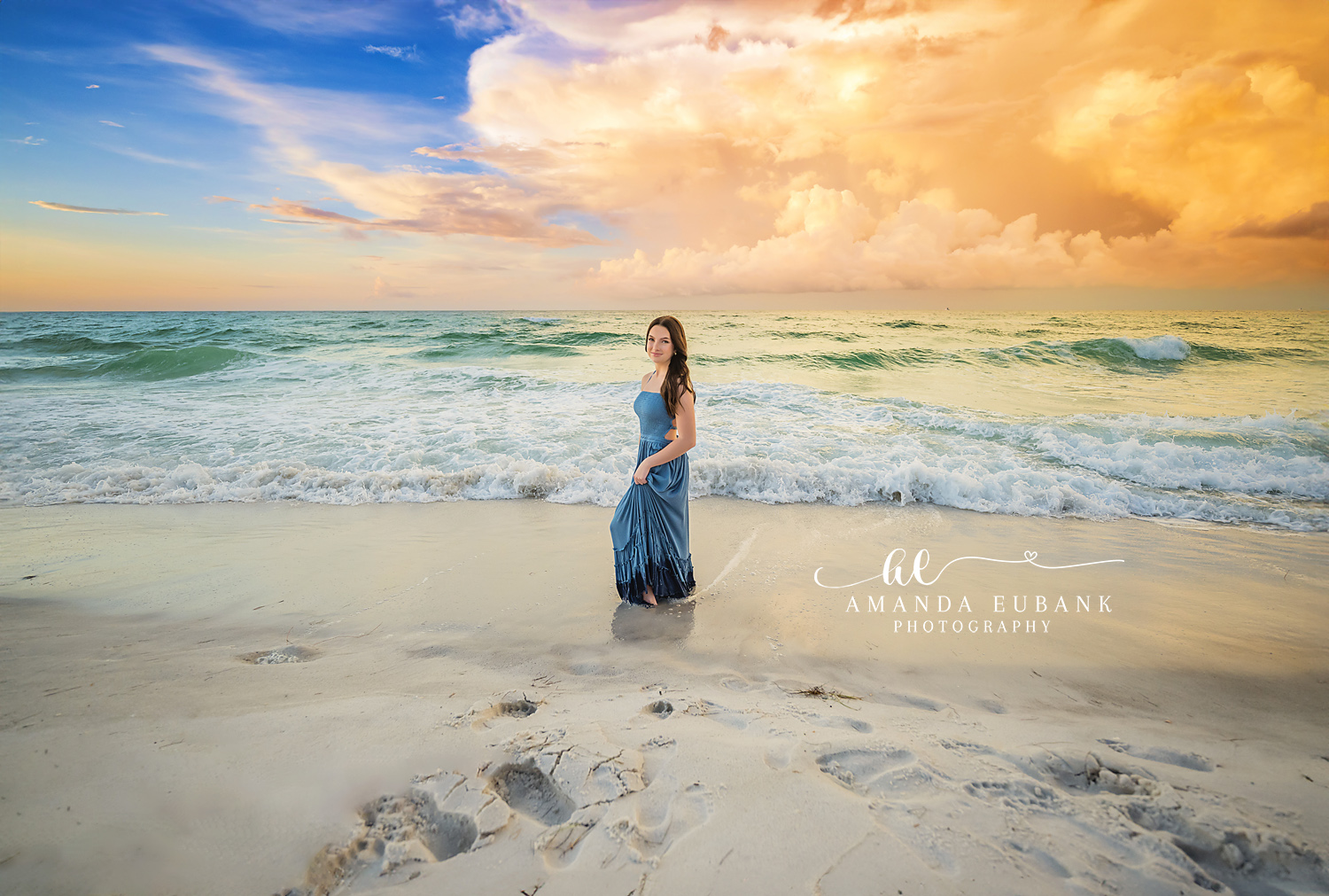 Towering Cloud Behind Her | Tampa Senior Photographer A senior in a blue skirt on the sand beneath a towering golden thunderhead during a senior portrait session in Tampa, Florida.
