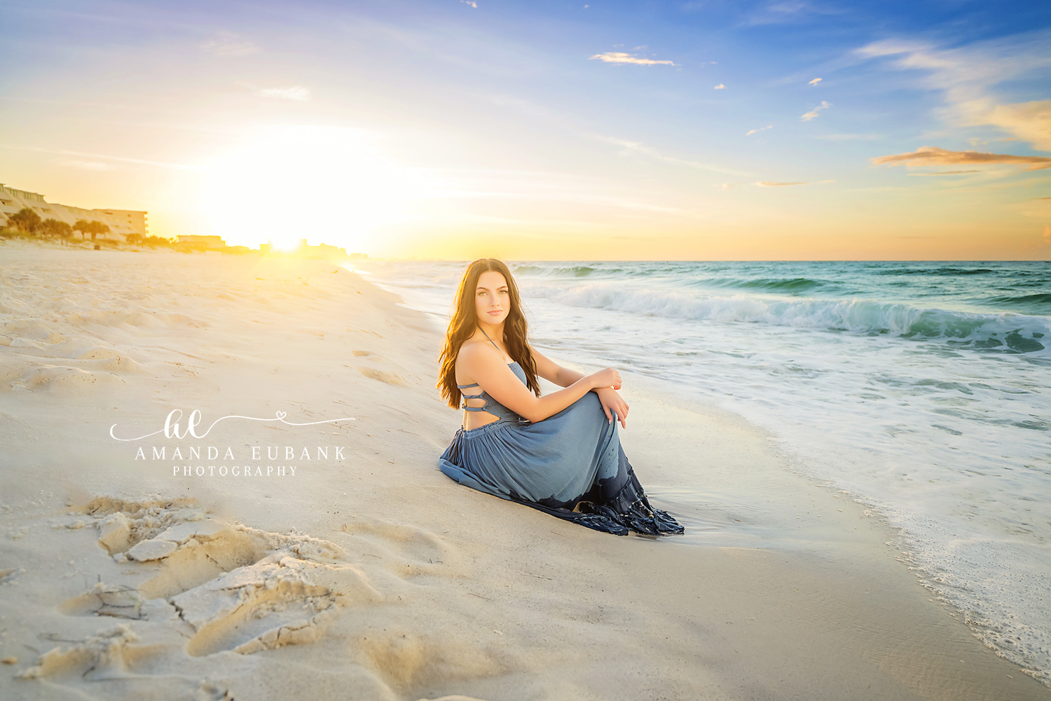 Sunburst Over the Shoulder — Tampa Bay Senior Photography A senior seated on the sand as the sun bursts along the shoreline behind her at a beach senior session in Tampa, FL.