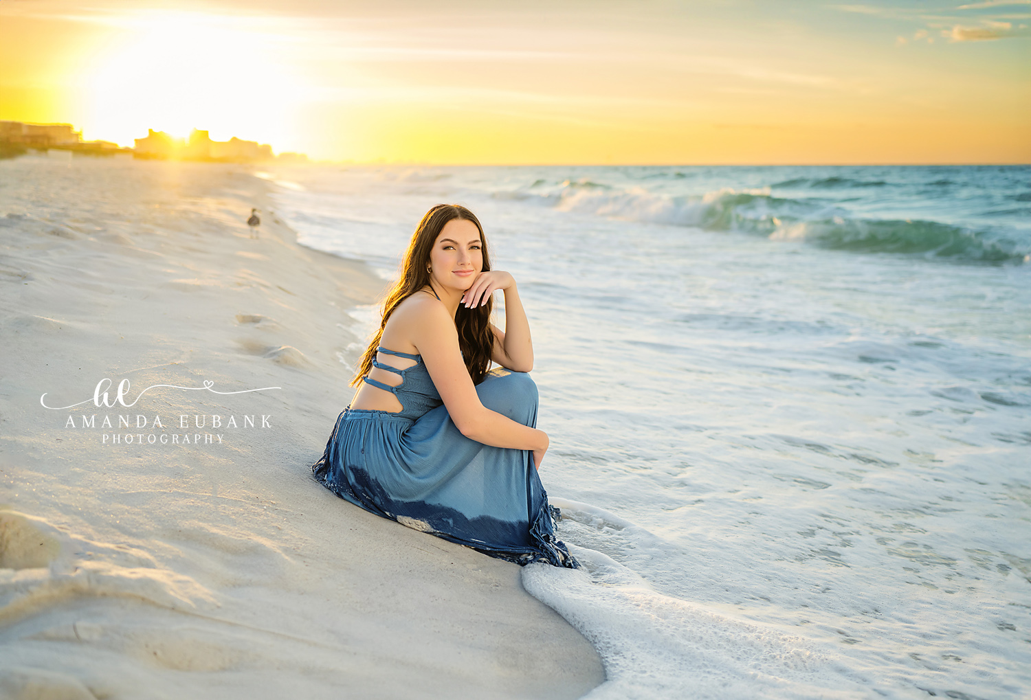 Backlit on the Beach | Beach Senior Session in Tampa, Florida Senior pictures in Tampa Bay showing a backlit senior in a blue skirt seated on the sand with the sun low behind.