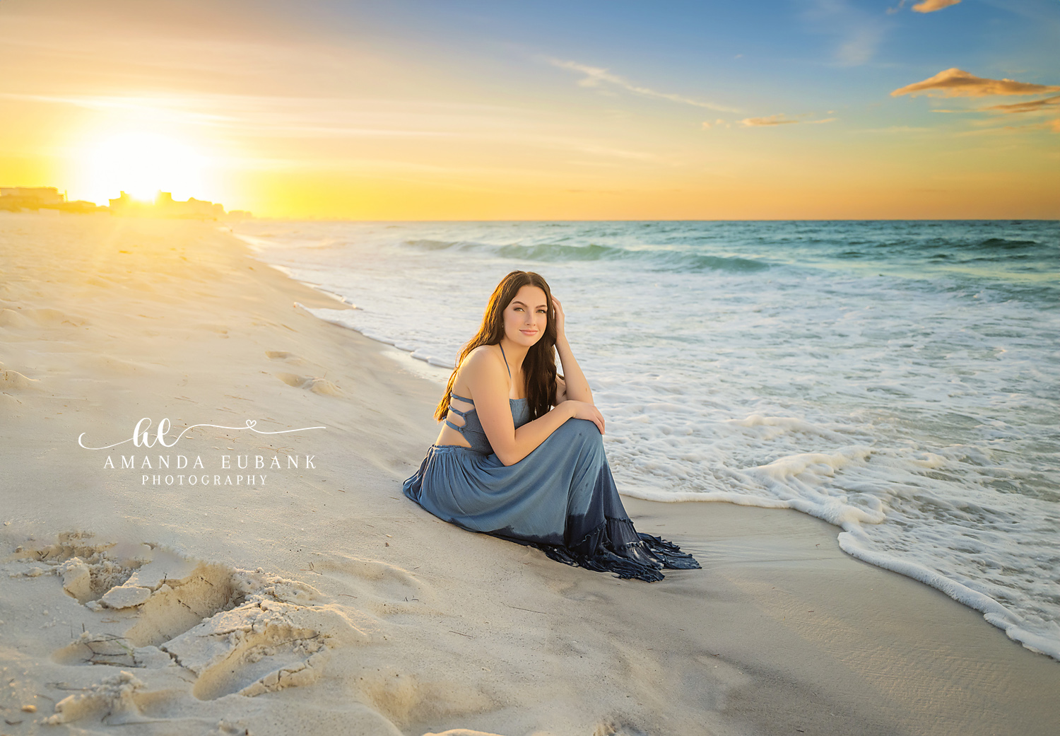 Sun on the Water Behind Her | Senior Portraits in Tampa, FL Tampa senior photographer captures a senior in a blue skirt seated on the shoreline with the sun low on the Gulf.