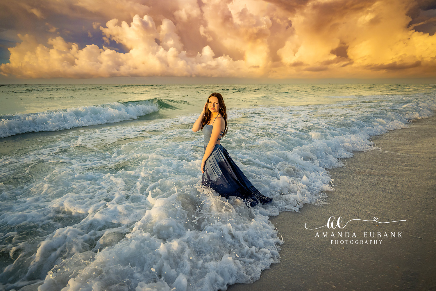 Navy Gown in the Surf | Beach Senior Session in Tampa, Florida Senior pictures in Tampa Bay showing a senior in a navy gown in the breaking surf beneath towering golden clouds.